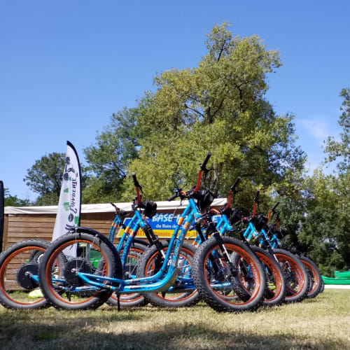 Vélos-cargo bleus aux roues rouges alignés devant le Logis des Tourelles à Cognac, arbres en arrière-plan