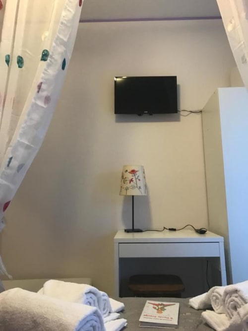 Camera d'albergo con TV a parete, lampada decorativa sulla scrivania, asciugamani arrotolati e opere floreali presso RL GROUP B&B