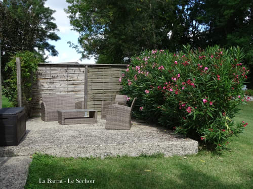 Cozy garden seating area at La Barrat cottage Le Séchoir with wicker furniture, flowering pink bushes, and wooden fence in