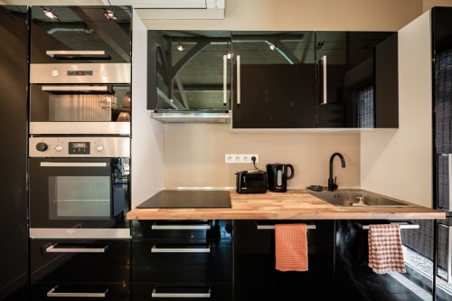 Cuisine moderne avec armoires noires, plan de travail en bois, appareils électroménagers en acier inoxydable et évier à Villa Eden Bleu