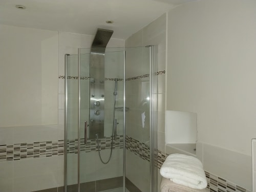Modern bathroom with glass shower enclosure, white tile walls, and decorative mosaic tile stripe at La Barrat cottage in