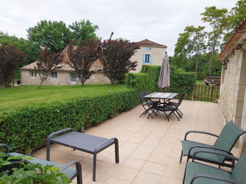 Patio at La Crèche cottage in Monmarvès with dining table, loungers, and stone house beyond hedges