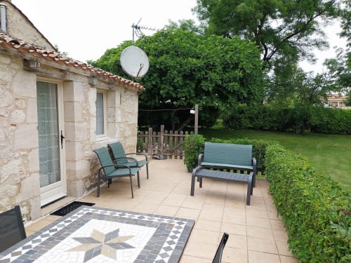 Patio seating area at La Crèche cottage in Monmarvès with stone building, lounge chairs, and lush green garden