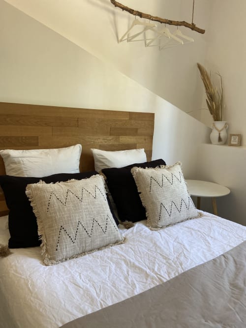 Modernes Schlafzimmer im Mas Lafleur mit Holzkopfteil, weißer Bettwäsche, geometrisch gemusterten Kissen und minimalistischer Einrichtung