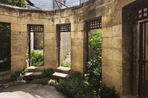 Cour historique en pierre de l'Hôtel La Prison à Béziers avec porches voûtés et verdure luxuriante