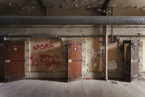 Cellules de prison abandonnées aux portes rouges de l'Hôtel La Prison à Béziers, France, avec murs usés et tuyauteries industrielles.