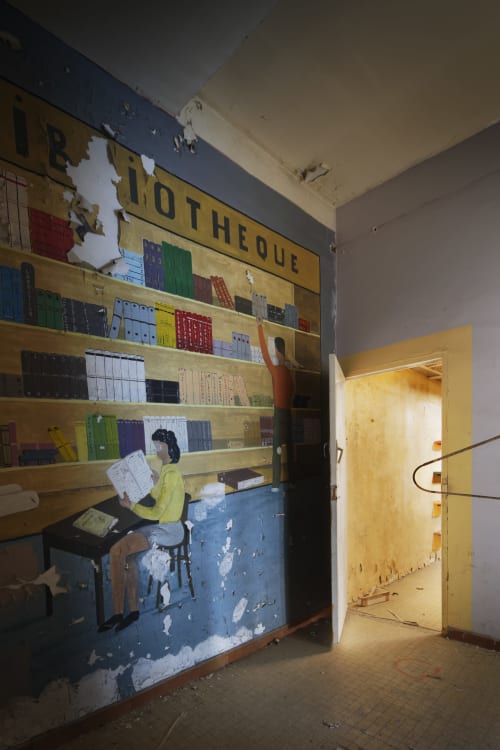 Bibliothèque abandonnée à l'Hôtel La Prison de Béziers, avec étagères usées et porte jaune