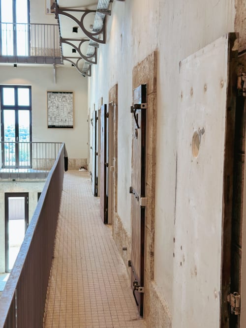 Corredor histórico de la Cárcel del Hotel La Prison Béziers con puertas de celdas individuales y muros de piedra vista