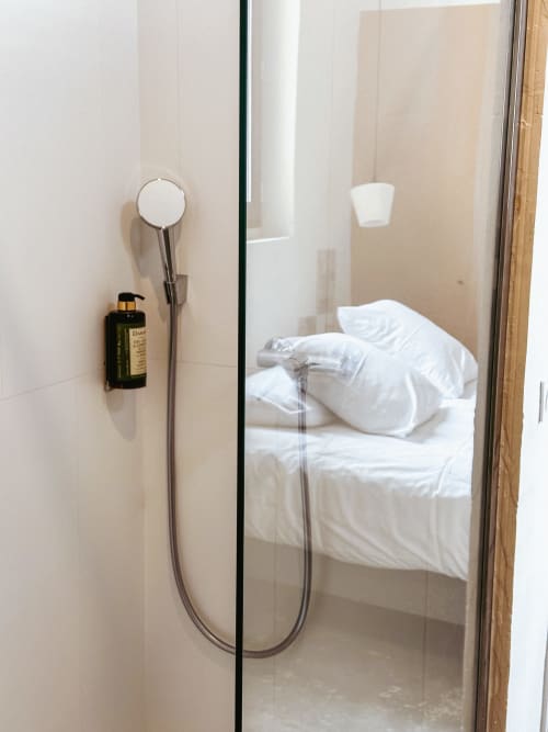 Mampara de ducha de cristal con alcachofa cromada y dispensador de jabón oscuro en el Hotel La Prison de Béziers, Francia