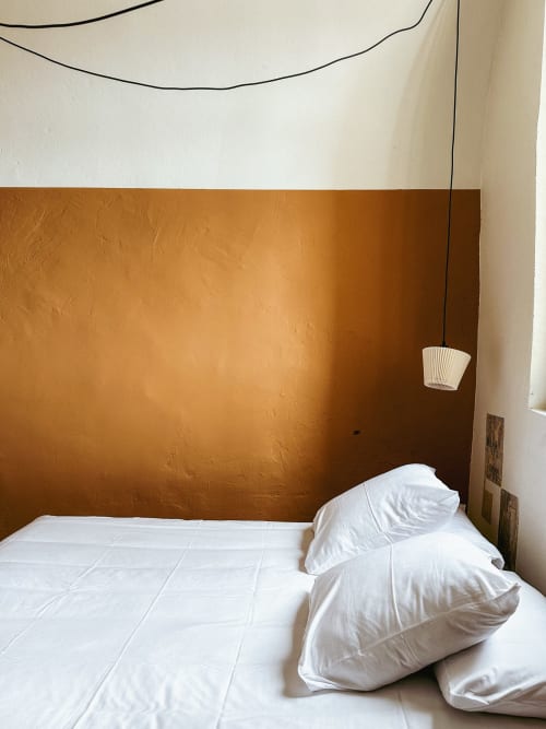 Habitación de hotel minimalista en La Prison Béziers con pared de acento naranja, ropa de cama blanca y dos almohadas