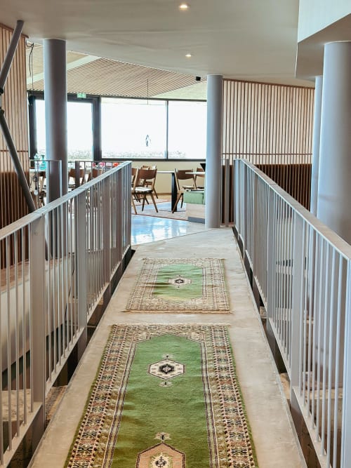 Pasillo moderno del hotel La Prison con barandillas metálicas, alfombras con motivos verdes y ventanales panorámicos con vistas a Béziers