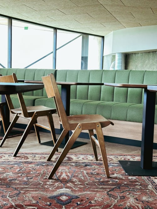 Área de descanso moderna en Hotel La Prison Béziers con sillas de madera de mediados de siglo, banqueta verde, mesas oscuras y patrones