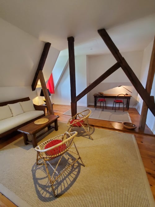 Gezellige retro zolder in Logis des Tourelles te Cognac met zichtbare balken, rotan stoelen en crème meubels