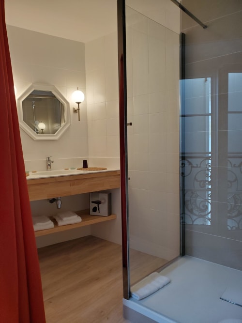 Salle de bains moderne du Logis des Tourelles B&B à Cognac avec douche à l'italienne, vasque en bois, miroir octogonal et rideau rouge
