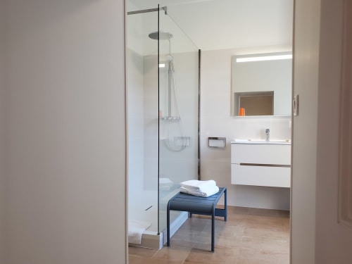 Salle de bains moderne du Logis des Tourelles B&B à Cognac avec douche vitrée, lavabo blanc et banc noir