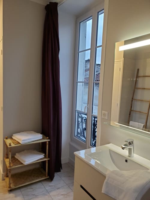 Salle de bains moderne au Logis des Tourelles B&B à Cognac avec lavabo, miroir, porte-serviettes et portes-fenêtres donnant sur les toits