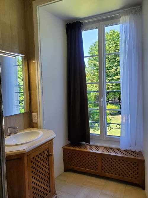 Salle de bain avec lavabo, mobilier en bois et portes vitrées donnant sur les jardins verdoyants du Logis des Tourelles, Cognac