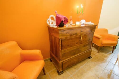 Elegante camera arancione con cassettone in legno, sedia rossa, candelabro e decorazione cuore alla Locanda degli Illustri B&B