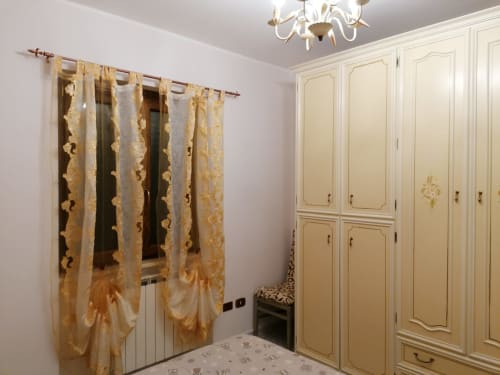 Camera elegante nell'appartamento di Civitanova del Sannio con armadio color crema, tende dorate decorate, lampadario e finiture bianche