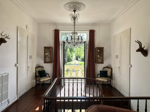Élégante entrée du Manoir Le Coutureau avec lustre, chaises anciennes et vue sur le jardin par les portes-fenêtres