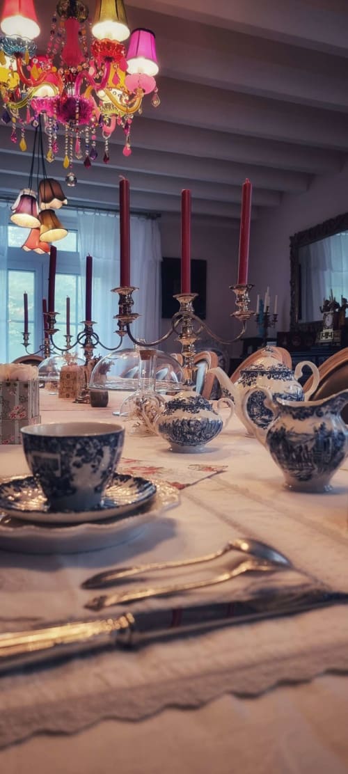 Table de salle à manger élégante au Manoir Le Coutureau avec théières en porcelaine bleue, chandeliers et lustre rose orné.
