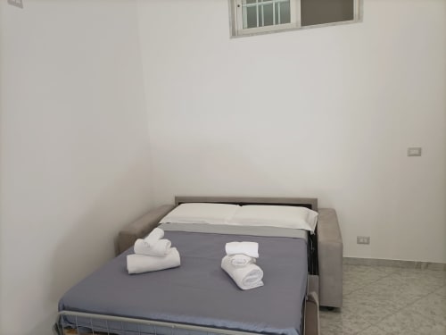 Camera da letto minimalista dell'appartamento Newhouse a Bari con letto grigio, cuscini bianchi e asciugamani arrotolati