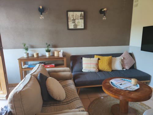 Salon moderne de la villa de Dinan avec fauteuil beige, canapé anthracite, table en bois et vue sur le jardin