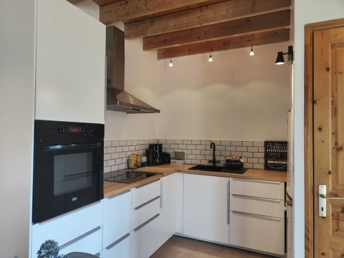 Cuisine moderne blanche avec poutres en bois et électroménagers inox à La Conciergerie de Nathalie, Dinan