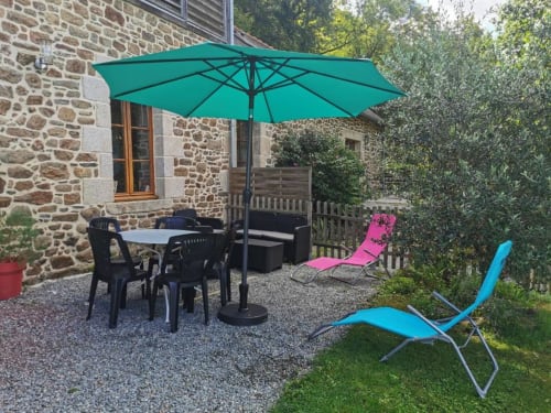 Parasol turquoise sur la terrasse de La Conciergerie de Nathalie à Dinan, vue sur le bâtiment en pierre et les jardins