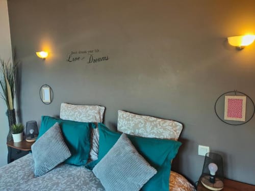 Chambre cosy à La Conciergerie de Nathalie à Dinan avec accents bleu-vert, coussins à motifs et décoration murale inspirante