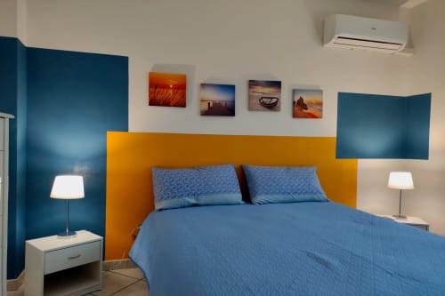 Camera da letto dell'appartamento costiero Stella Marina con letto blu, testata arancione, pareti turchesi e opera d'arte marina a Porto Empedocle