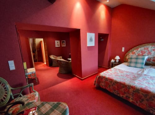 Chambre de la Junior Suite au Château d'Hassonville à Marche-en-Famenne avec murs rouges, literie à motifs floraux et équipements modernes