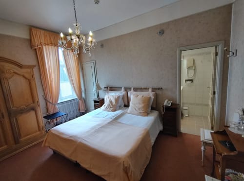 Chambre élégante du Château d'Hassonville avec lit double, lustre et salle de bains attenante à Marche-en-Famenne