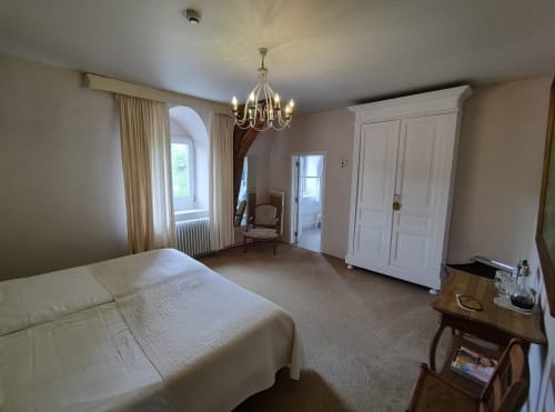 Spacieuse chambre du Château d'Hassonville avec lit queen-size, lustre, fenêtres cintrées, armoire et mobilier élégant