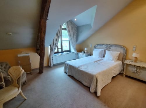 Chambre spacieuse du Château d'Hassonville avec lits jumeaux, plafond mansardé, lucarne et murs jaune chaleureux