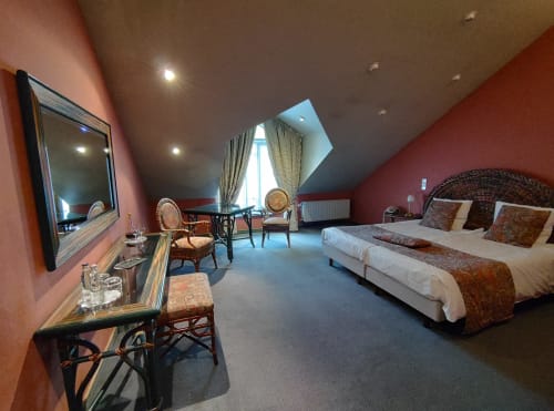 Chambre luxueuse du Château d'Hassonville avec lit double, murs rouges et coin salon près de la fenêtre