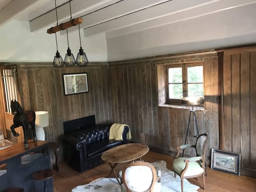 Coin salon rustique avec canapé en cuir foncé, murs en bois et luminaires suspendus au Petit Manoir de Kériolet