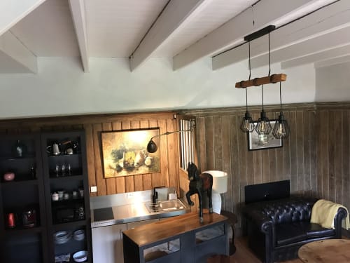 Intérieur de cottage moderne avec poutres apparentes, cuisine ouverte, sièges en cuir noir et luminaires suspendus au Petit Manoir de