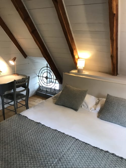 Chambre cosy sous les toits du Petit Manoir de Kériolet avec poutres apparentes, lit aux coussins gris, bureau et éclairage chaleureux