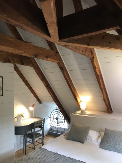 Chambre mansardée chaleureuse avec poutres apparentes, murs en lambris blanc, coin bureau et lit aux oreillers verts au Petit Manoir
