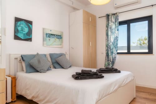 Chambre moderne à A Vida é Linda Santa Luzia avec lit blanc, oreillers bleus, vue sur le jardin et art mural contemporain.