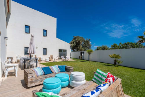 Spacieux jardin de villa avec bâtiment blanc moderne, terrasse en bois, sièges colorés et confortables, pelouse verte, palmiers