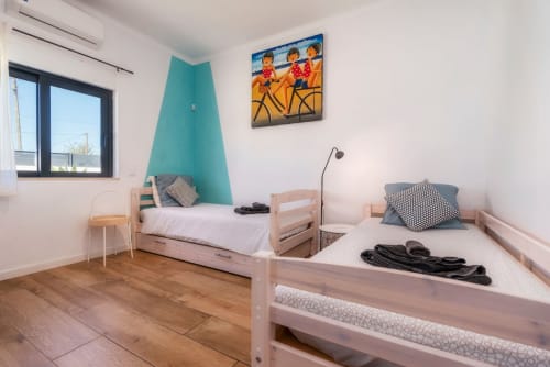 Chambre lumineuse avec mur d'accent turquoise, lits en bois et équipements modernes à la villa A Vida é Linda à Santa Luzia
