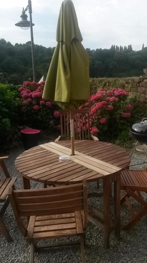 Table de salle à manger en bois avec parasol olive entourée de fleurs roses à la villa La Conciergerie à Dinan, France