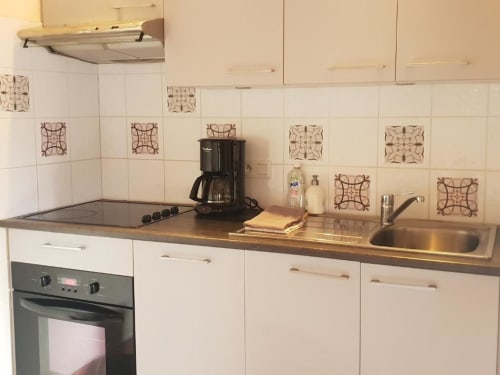 Cuisine contemporaine de la villa de Dinan avec meubles blancs, plan de travail foncé, cuisinière gaz, évier et dosseret carrelé