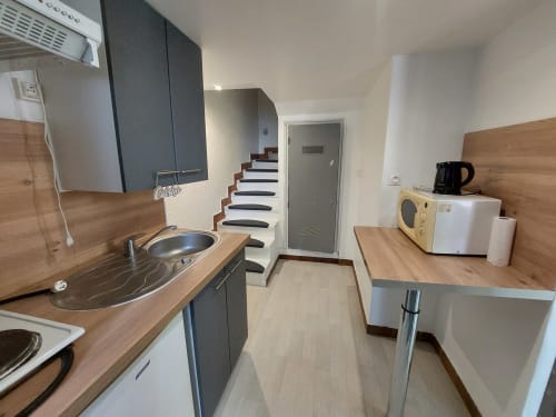 Cuisine moderne dans un appartement à Nancy avec comptoirs en bois, armoires grises, cuisinière et escaliers en arrière-plan