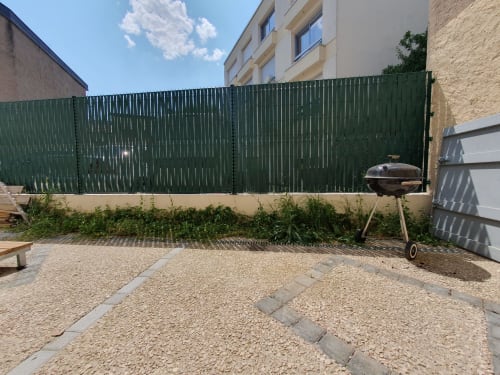 Terrasse extérieure de l'appartement NancyRoom à Vandoeuvre-les-Nancy avec clôture verte, barbecue et zone de détente gravillonnée