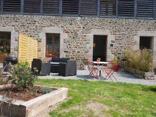 Cour de villa en pierre à Dinan avec espace de détente, chaises longues et table de bistrot rouge