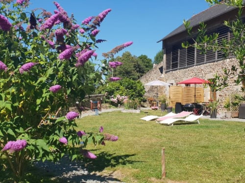 Des lilas mauves en fleur encadrent une cour de jardin ensoleillée à La Conciergerie de Nathalie à Dinan, avec espace détente