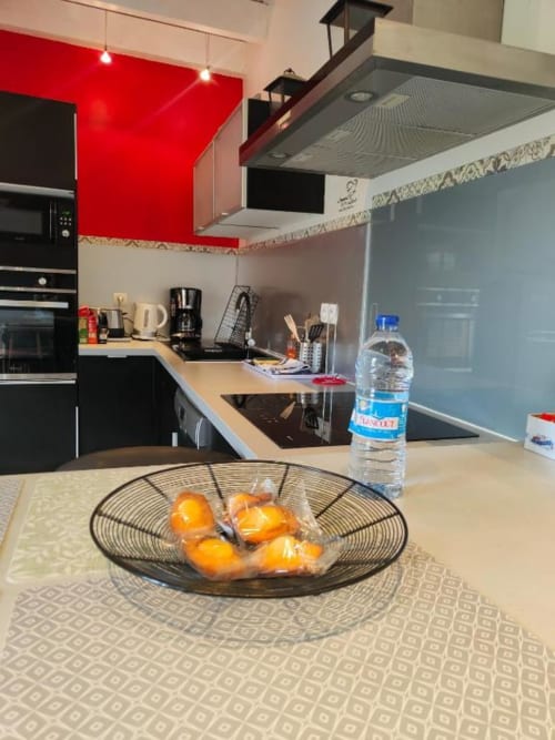 Cuisine moderne du Gîte de la Tannerie à Dinan avec armoires rouges, comptoirs noirs et oranges fraîches dans un panier métallique